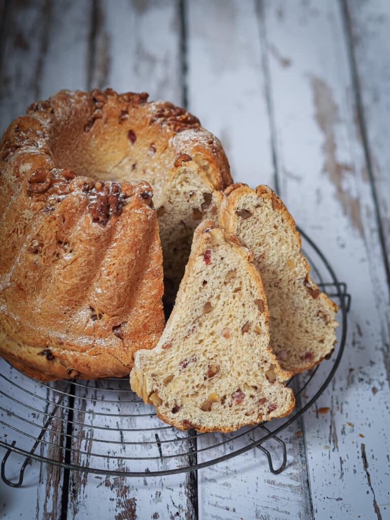 Kougelhopf salé noix et lardons sur une grille posé sur une planche en bois peinte en blanc et coupé en tranches. Mie bien visible