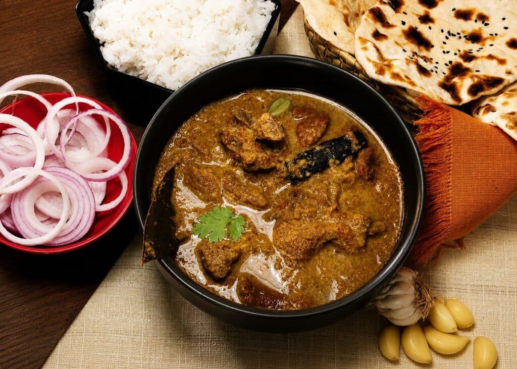Curry de viande dans un bol noir, riz blanc, naans et oignons rouges