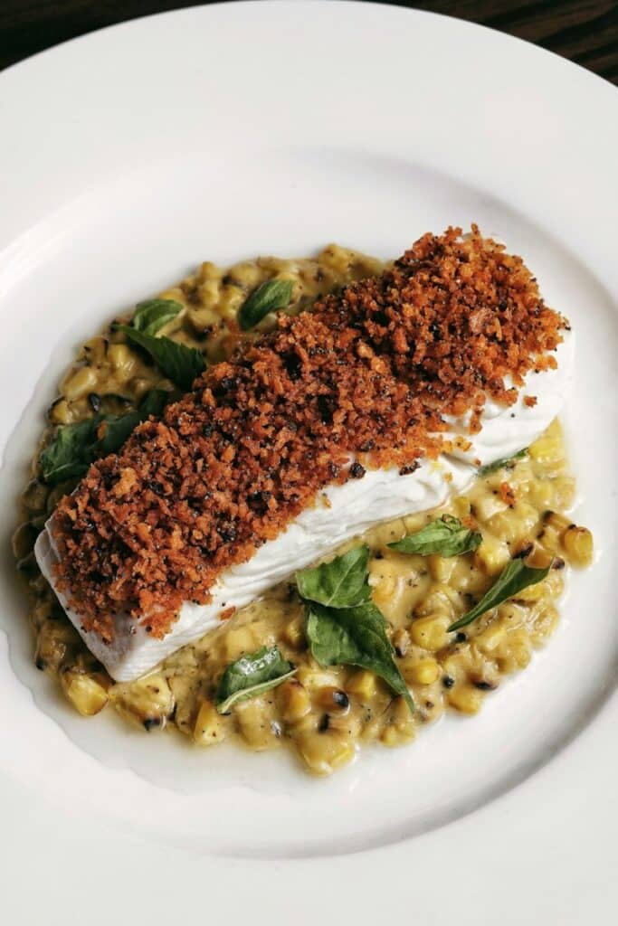 Filet de poisson blanc sous une croûte rouge-brun, servi sur des légumes