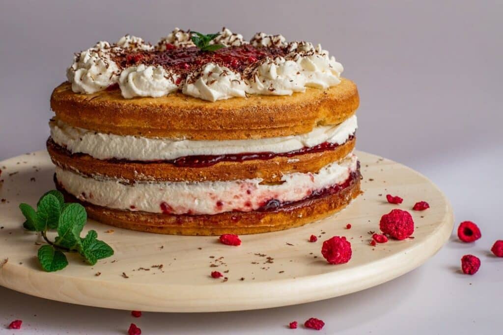 Gâteau à étages garni de crème fouettée et de confiture de framboises, framboises autour