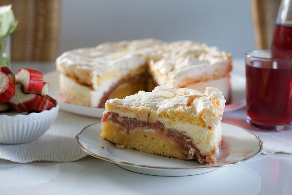 Part de gâteau à la rhubarbe meringué aux amandes effilées, tronçons de rhubarbe dans un bol