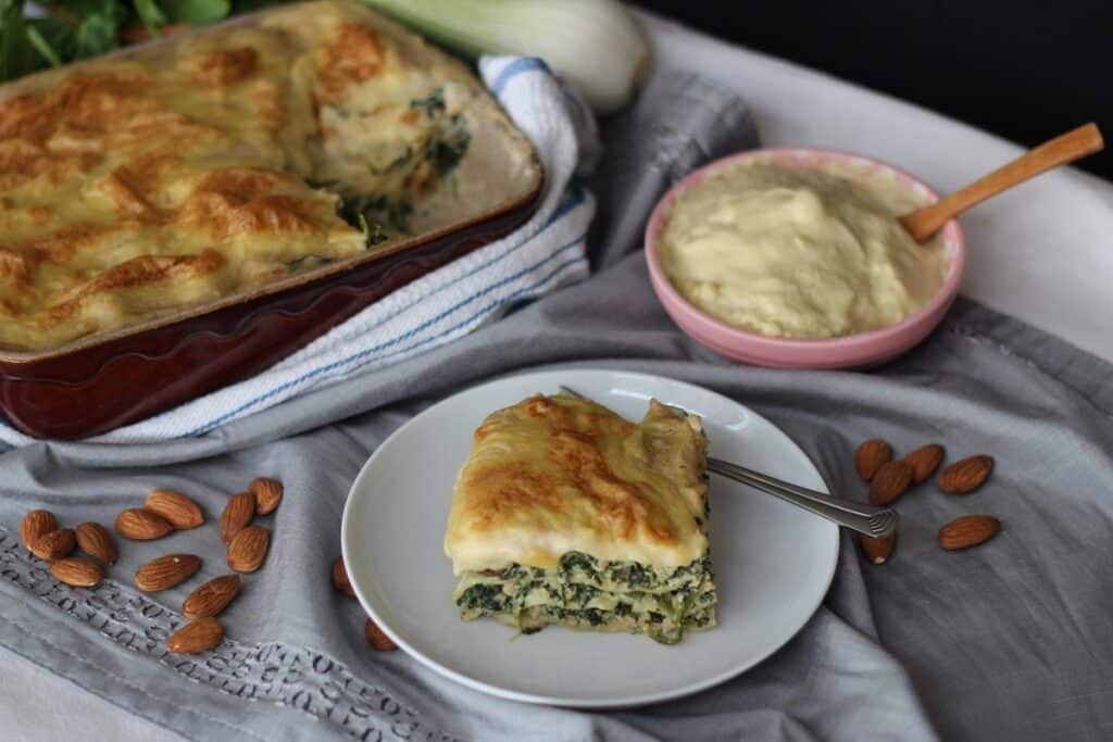 Part de lasagnes aux épinards et à la béchamel, plat de lasagnes en arrière-plan