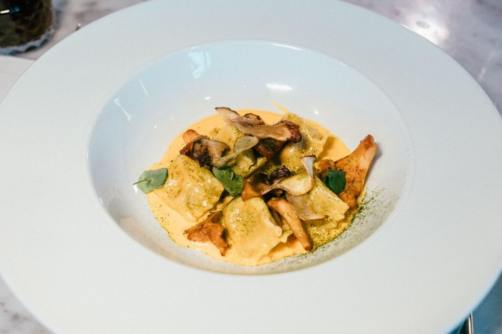 Ravioles aux champignons poêlés sur une sauce crémeuse, dans une assiette creuse blanche