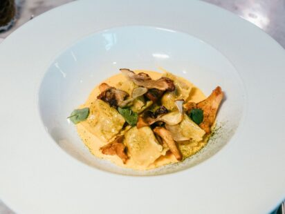 Ravioles aux champignons poêlés sur une sauce crémeuse, dans une assiette creuse blanche
