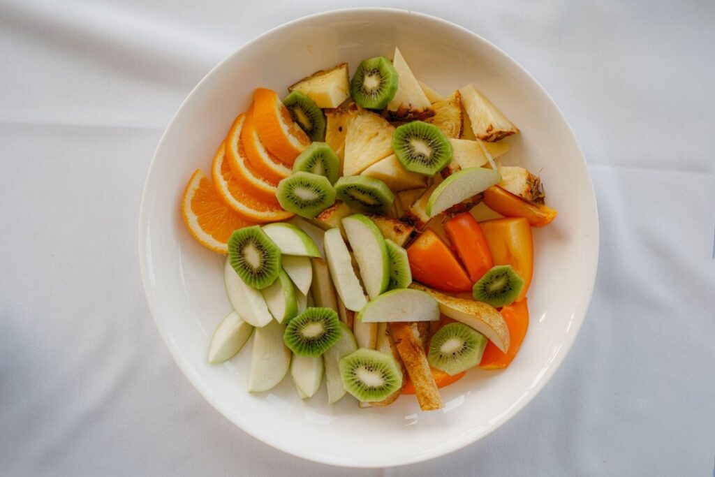 Salade de fruits frais dans un bol blanc : oranges, kiwis, pommes et ananas